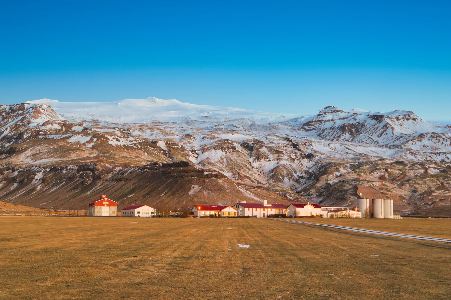 A Farm on yellow grass field in front of volcano eyjafjallajökullcovered in snow 
