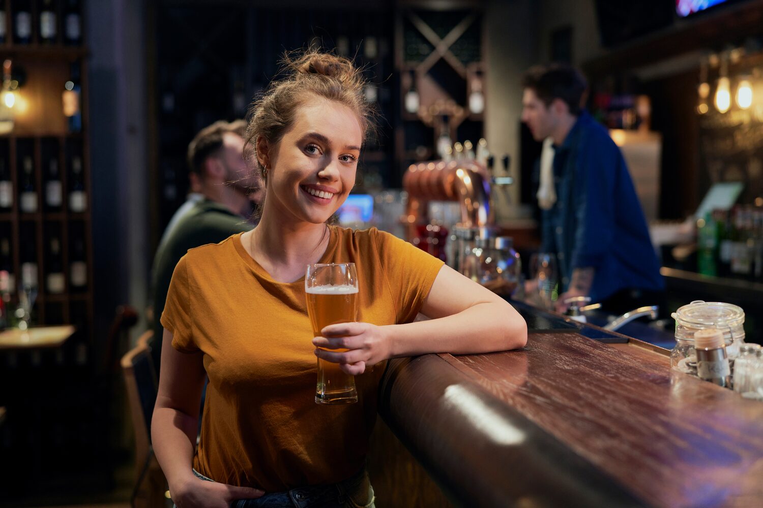 Portrait photo of smiling woman holding beer standing at the bar, bartender behind serving customer