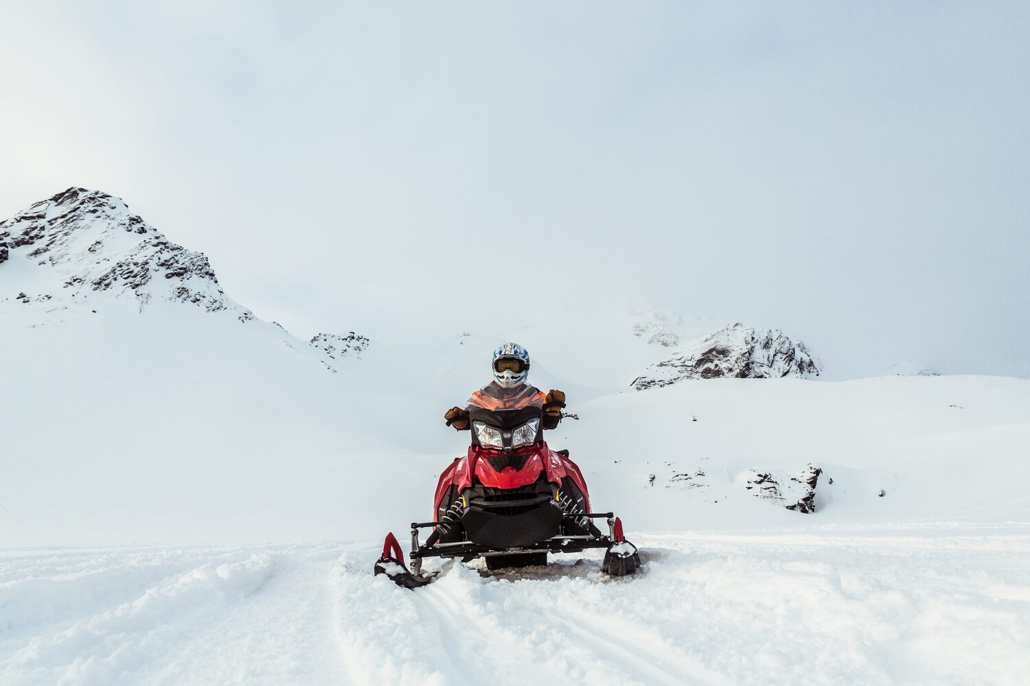Solo person on snowmobile driving in snow covered landscape with mountains in background