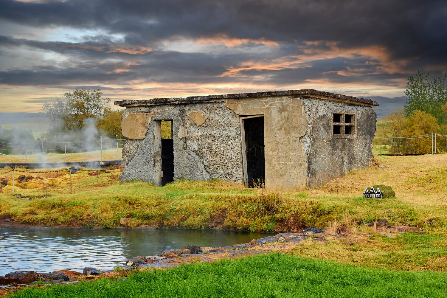 Historical building and ruins reflect on water in rural landscape, dark grey and pink clouds in sky 
