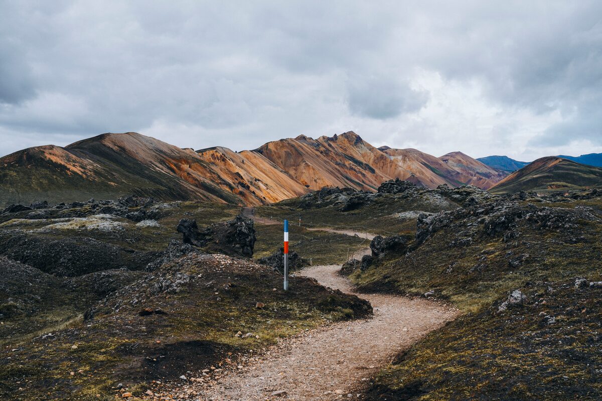 Hiking path surrounded by mountains with Icelandic flag poles to mark the way 