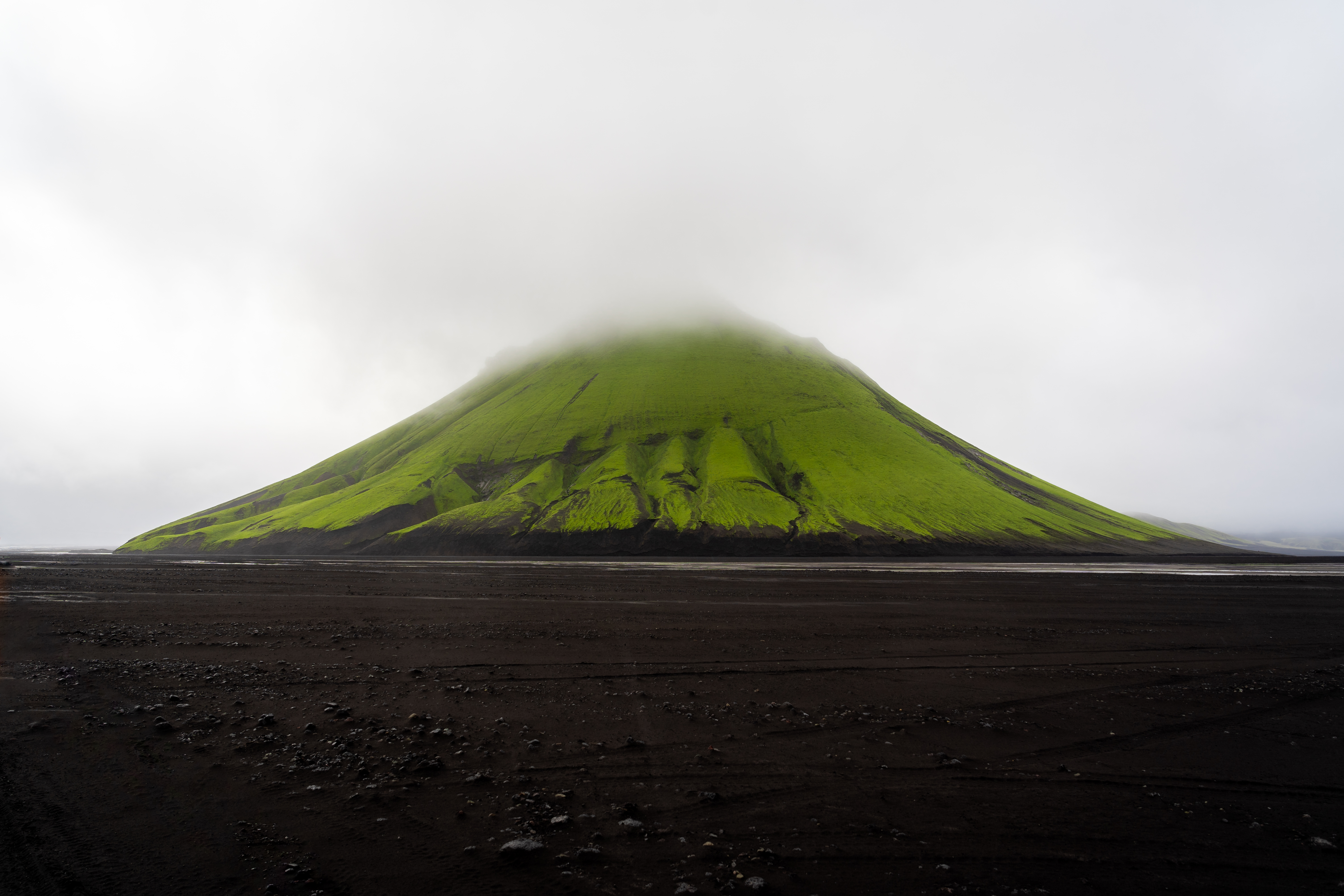 Vivid green mountain surrounded by black sand desert