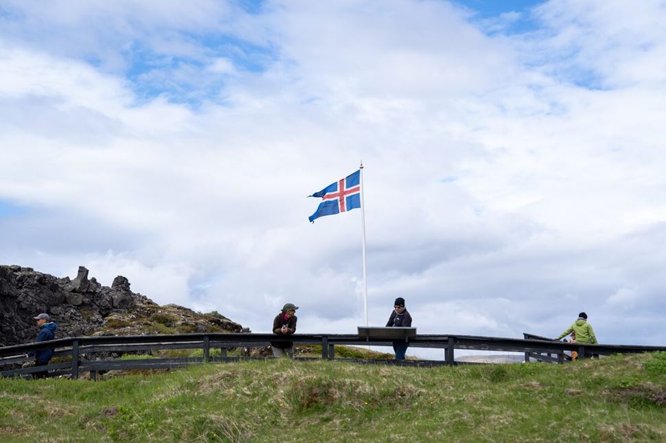 Thingvellir Icelandic Flag 3 tourists reading and enjoying sites at Thingvellir park, standing by Icelandic flag