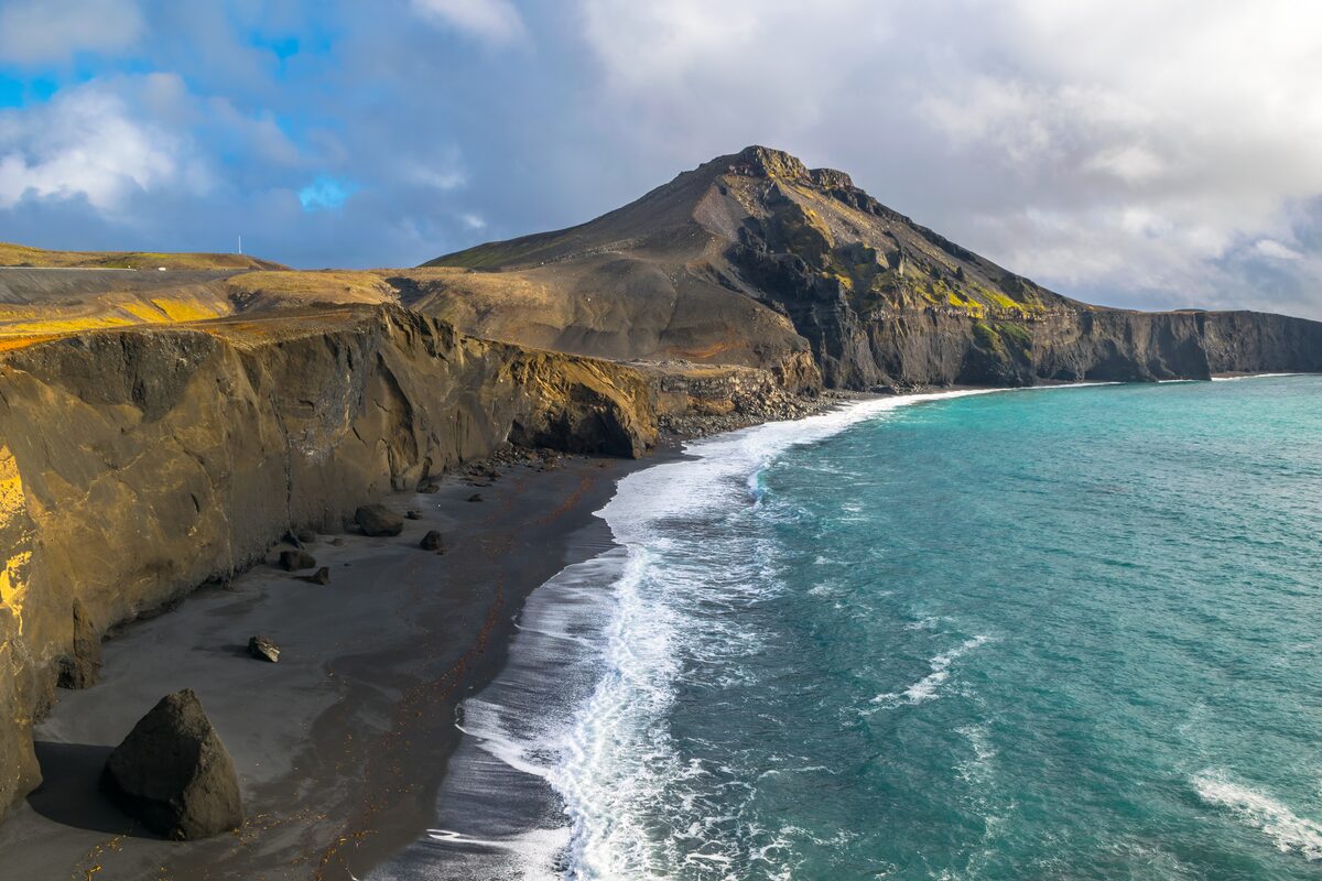 Rugged green cliffs next to coastal line and black sand beach in Iceland 