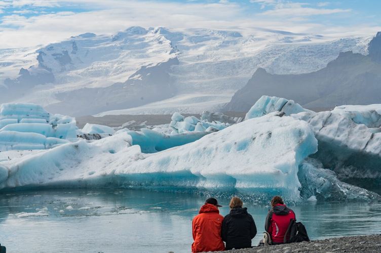 Three people sitting near glacier lagoon in Iceland