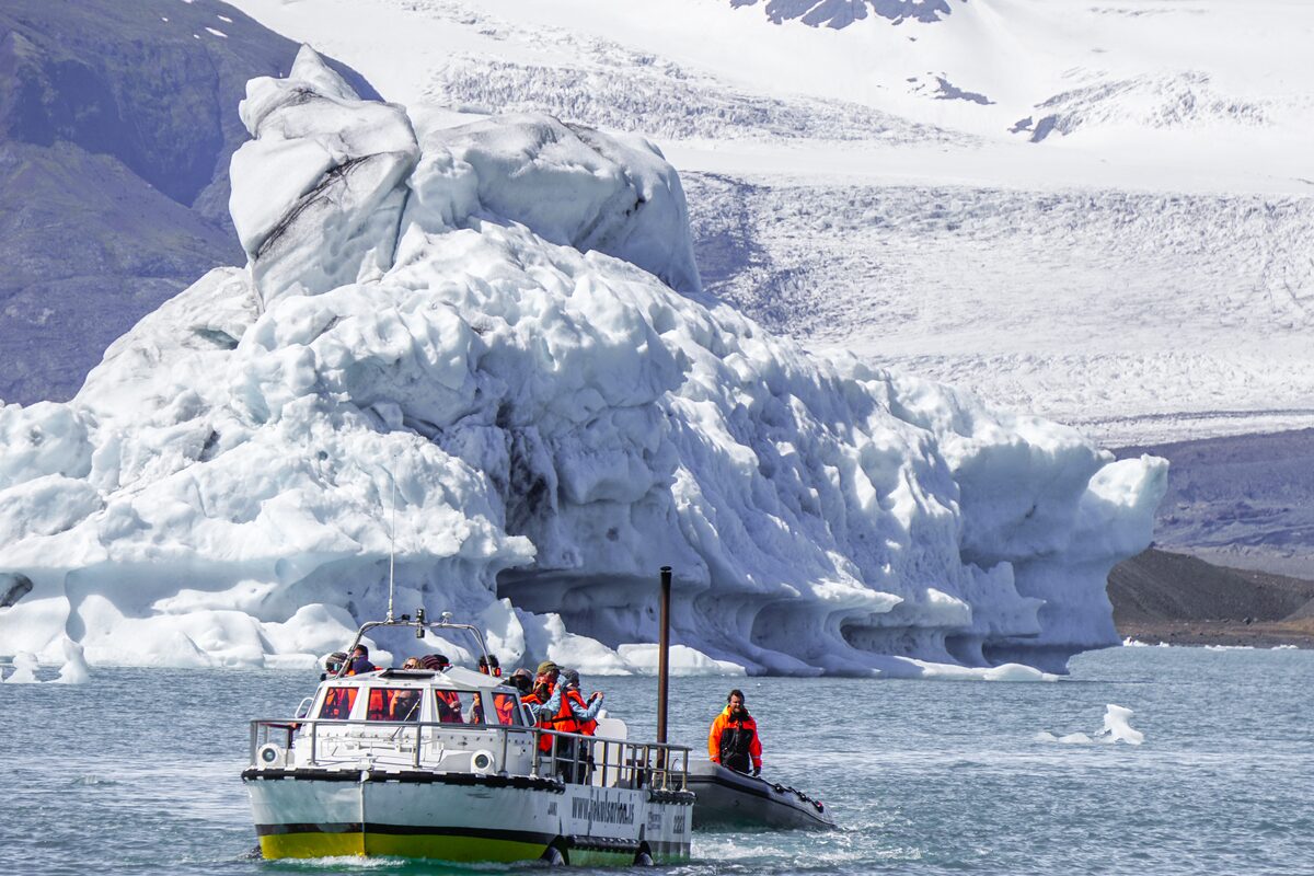 Boat swimming by huge iceberg