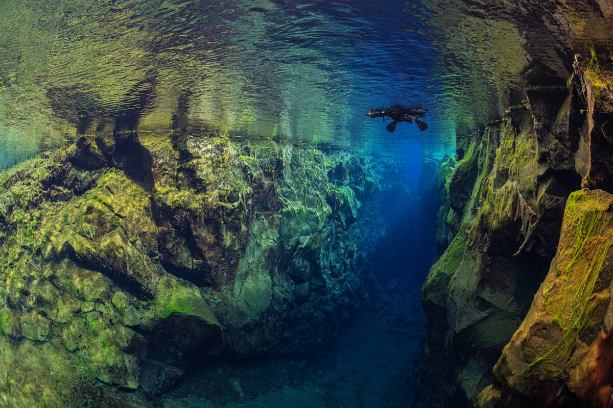 Person snorkeling by surface in clear blue waters by rocks