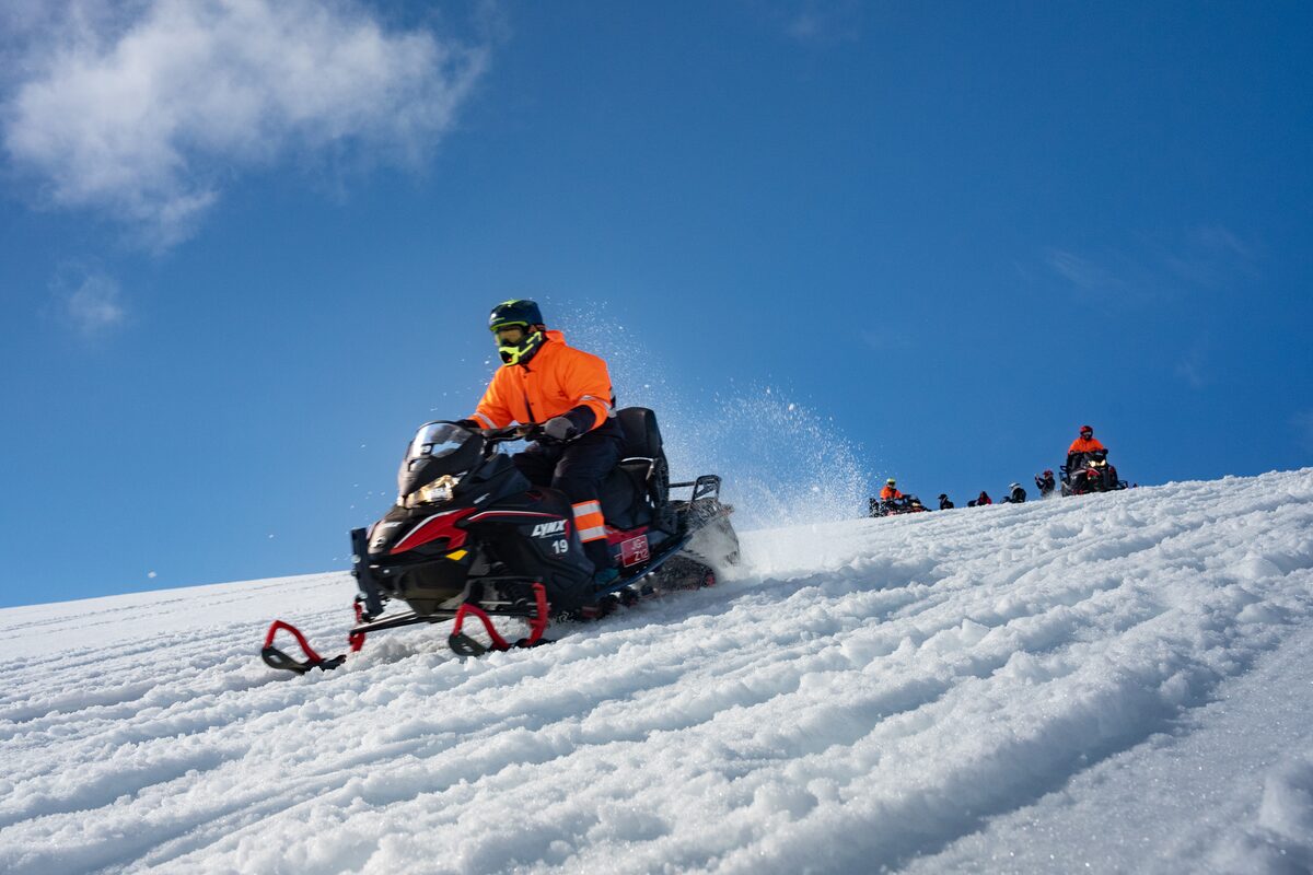 Snowmobile tour group snowmobiling down snow slope