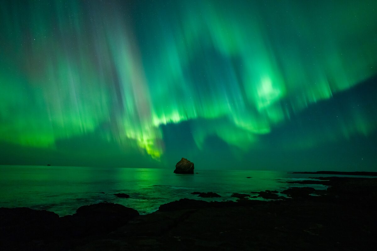 Green northern lights over rock in sea in Iceland.