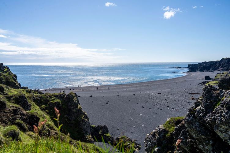 Scenic view of Djúpalónssandur black sand beach in Iceland, with dramatic lava rock formations, dark volcanic sand, and the waves crashing under a cloudy sky.