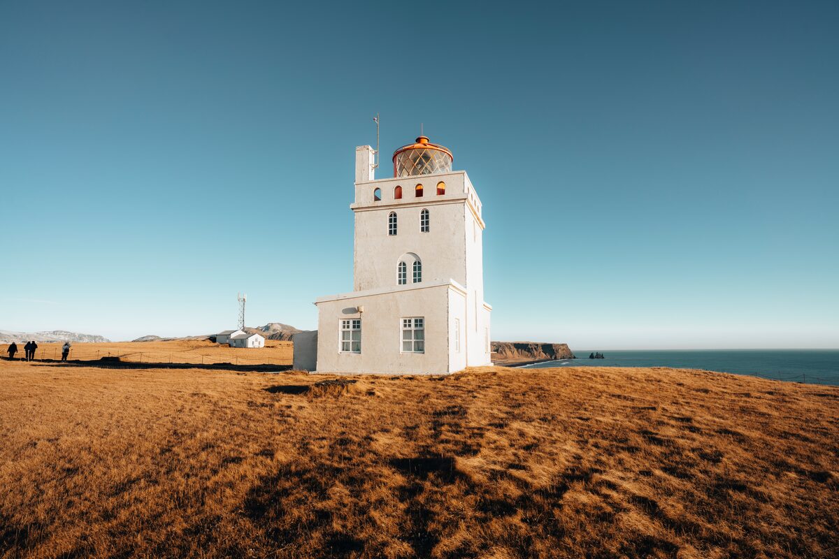 White lighthouse on edge of autumn grass next to the sea with bright blue skies