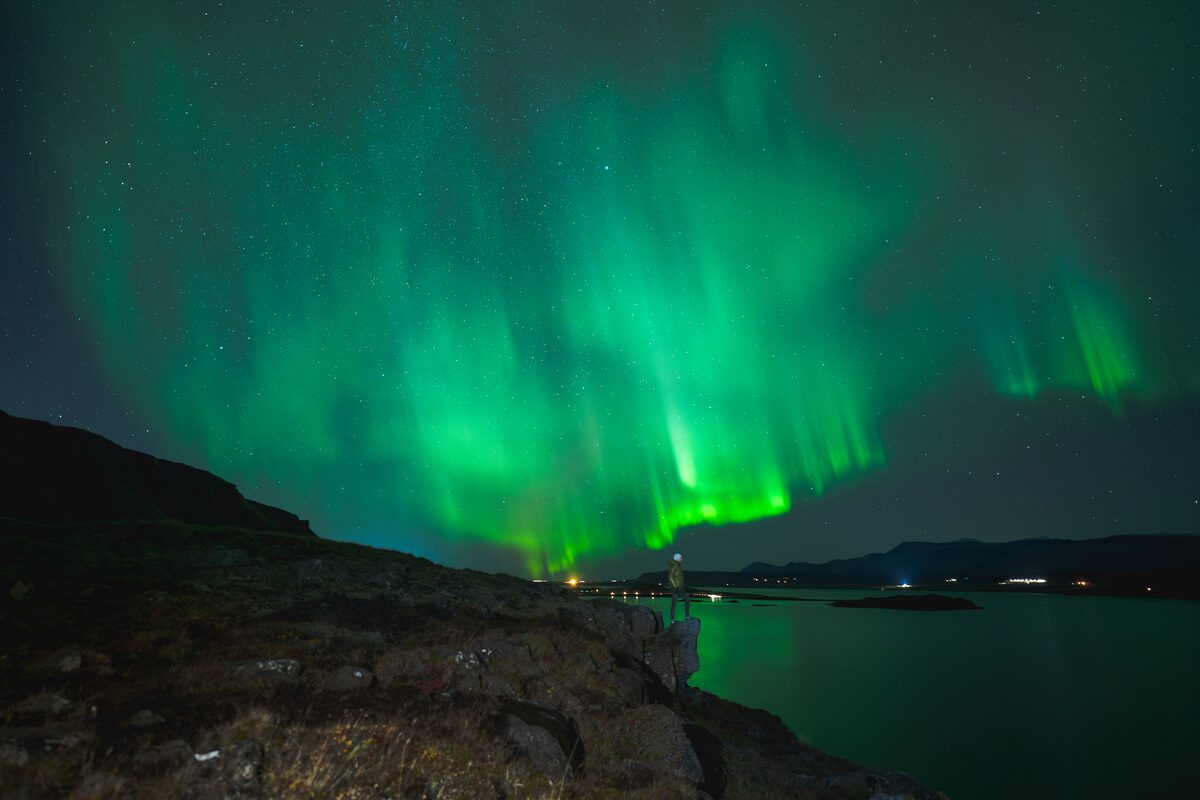 Man standing on rock by sea shore with Aurora in sky