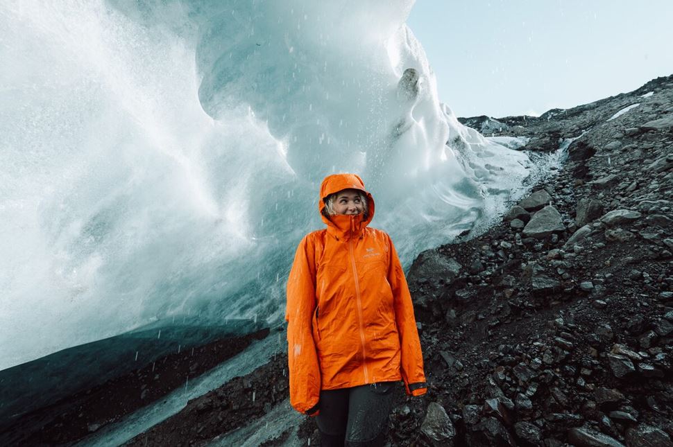 Woman in orange jacket standing in the rain in the area of the glacier