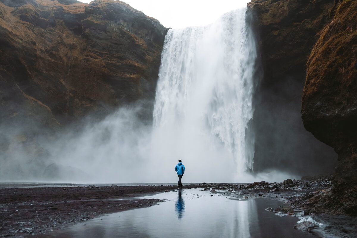 Tourist standing in front of skogafoss waterfall in blue coat  