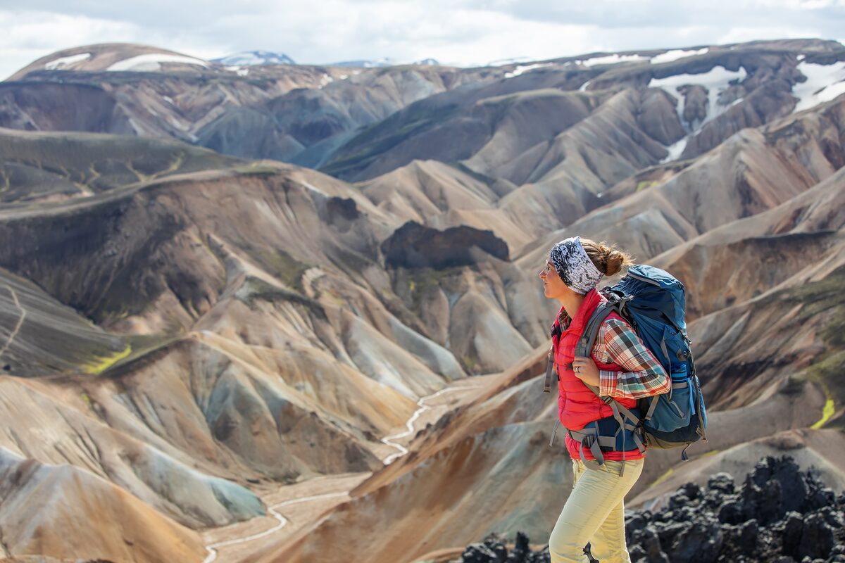 Women is standing on the Icelandic hills dressed in hiking attire.