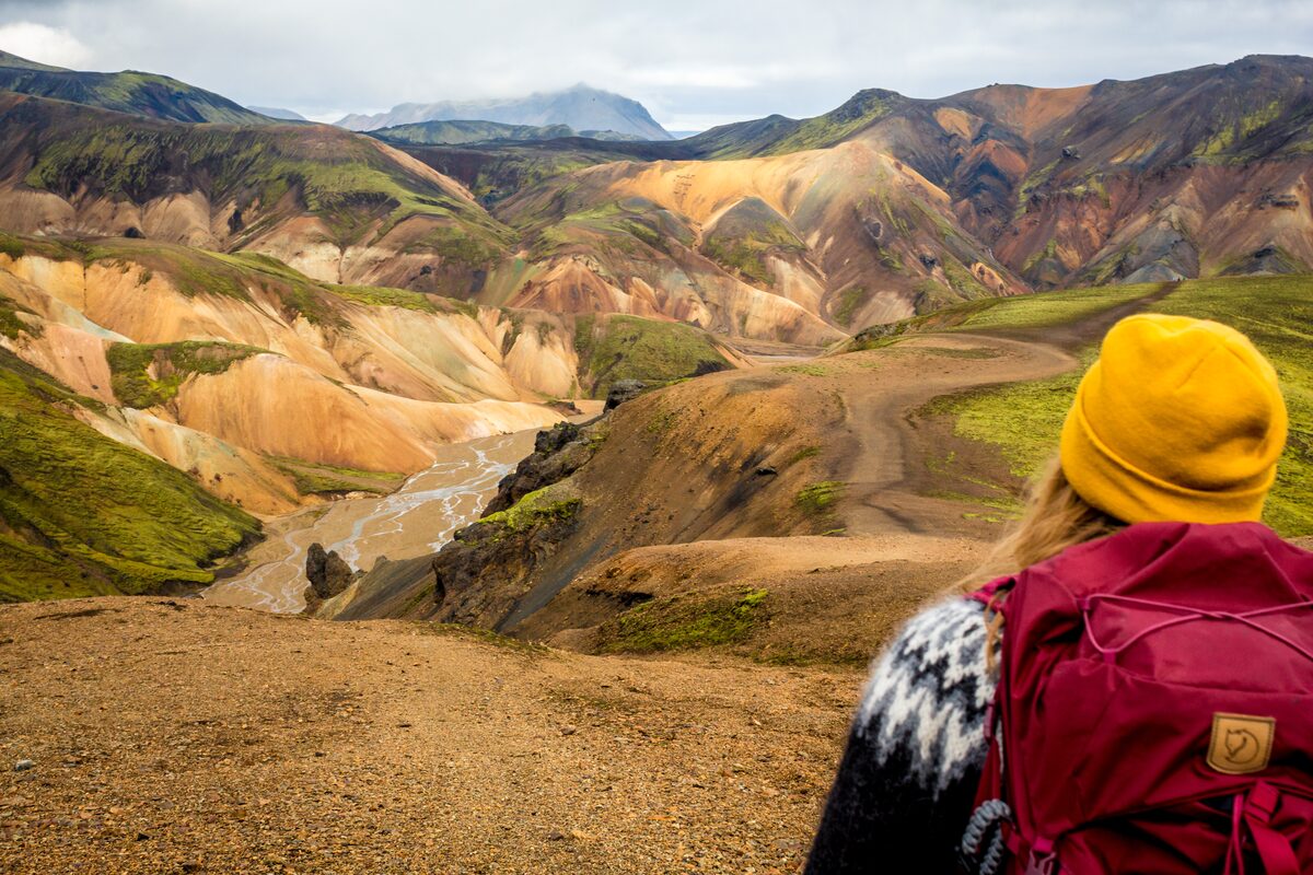 Woman with yellow hat and red backpack in mountains
