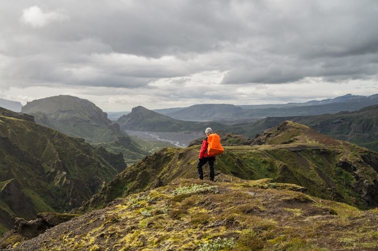Man with orange backpack and jacket standing at highest mountain peak