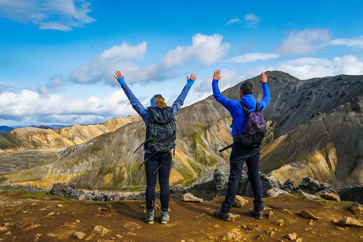 Two happy hikers standing in front of Landmannalaugar mountains with arms up