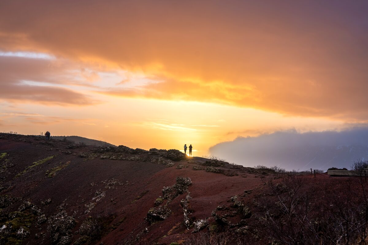Tourists on edge of volcanic crater lake during orange purple golden sunset