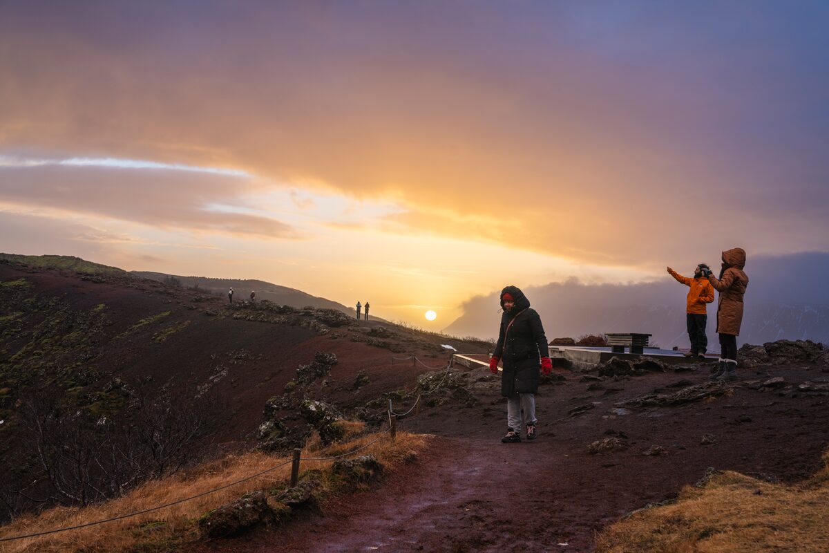 Tourists walking around edge of kerid volcanic crater lake during beautiful sunset