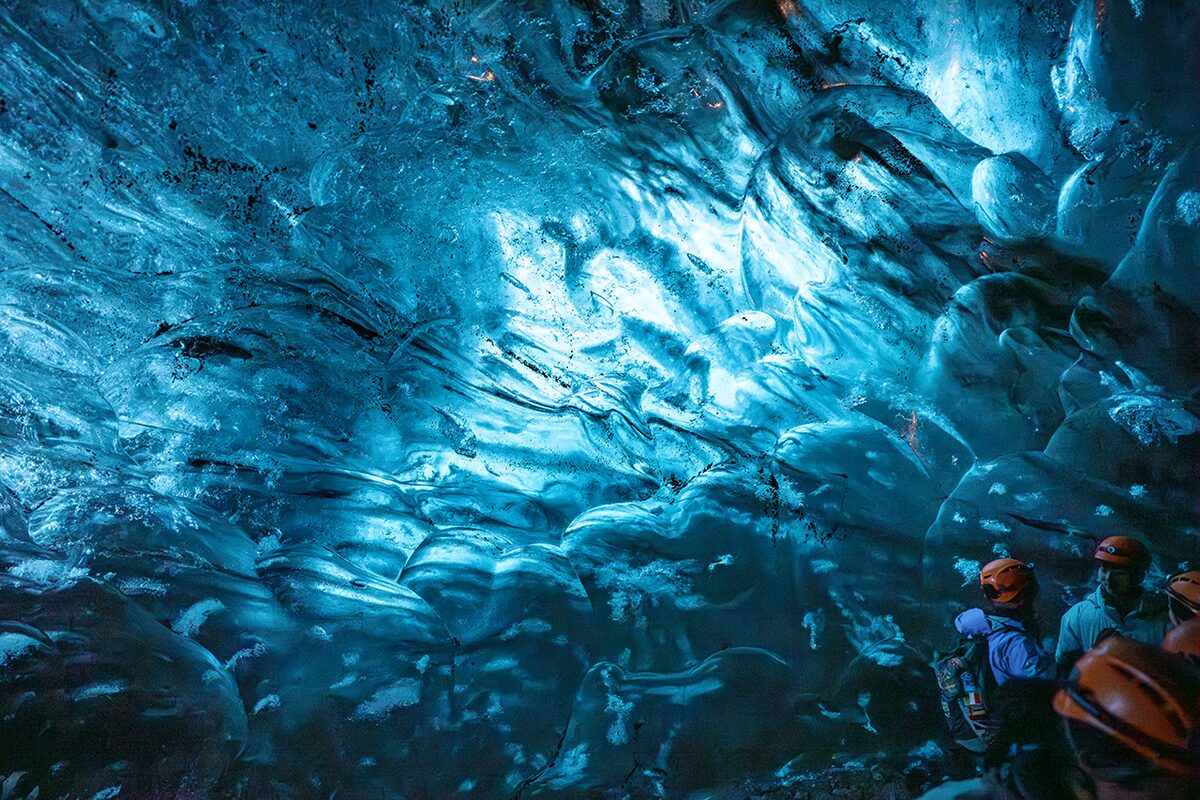 Blue Crystal ice cave wall patterns and tourists with safety helmets inside