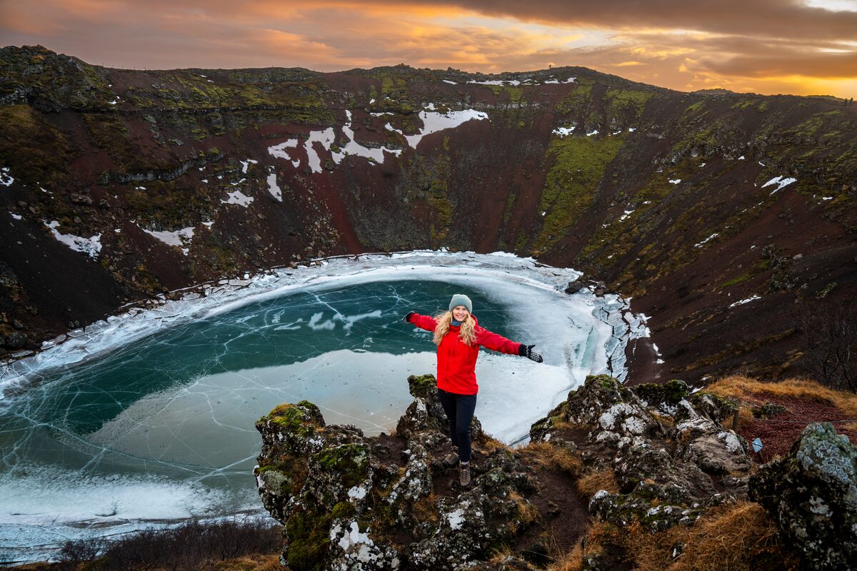 Tourist posing for photo by frozen Kerid crater lake in winter sunset