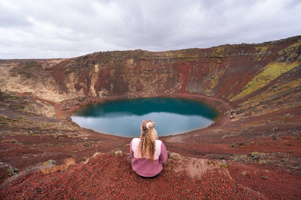 Female tourist in pink jumper sitting edge of Kerid crater lake admiring views