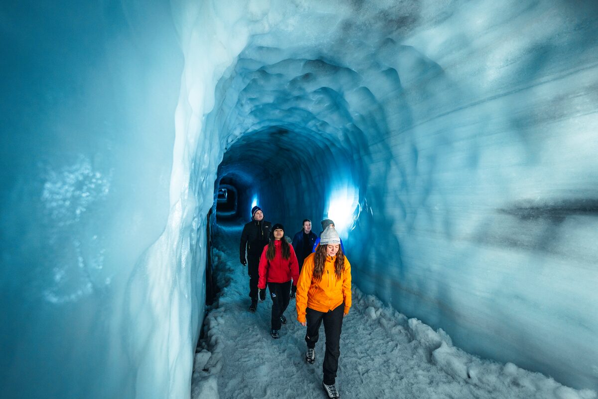 Small group tour people walking through glacier ice tunnel admiring view