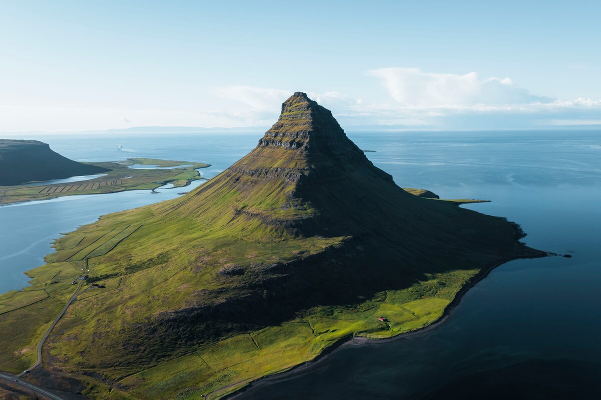 Ariel view of green Kirkjufell mountain surrounded by water and clear blue skies
