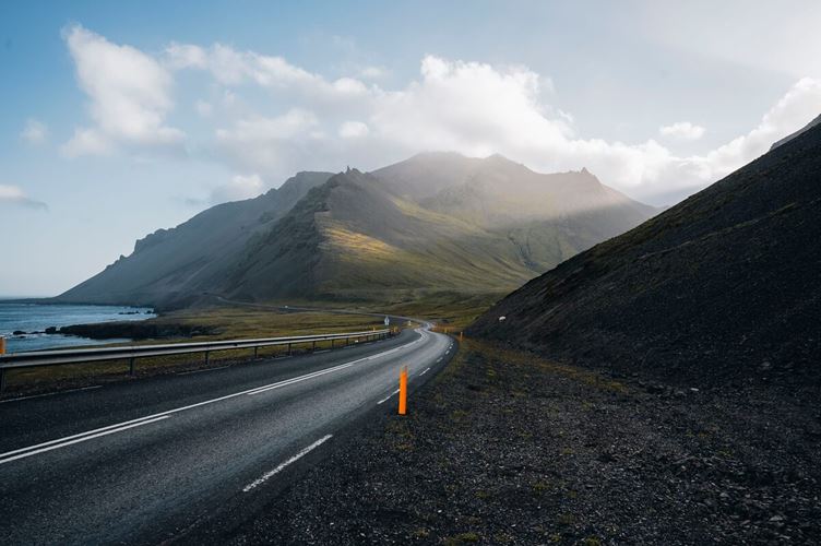 View of winding coastal road to green moss covered mountain in Iceland