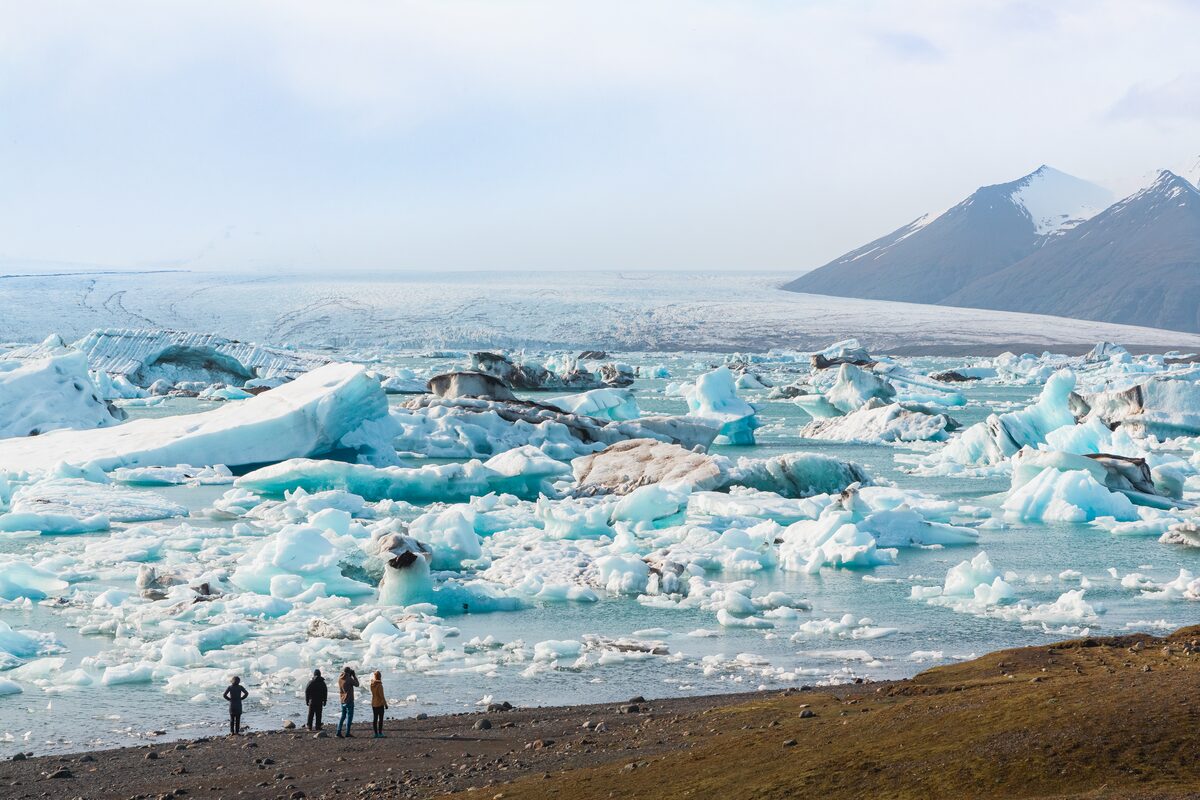 Group of four friends standing on the coast huge floating icebergs blue and black stripes