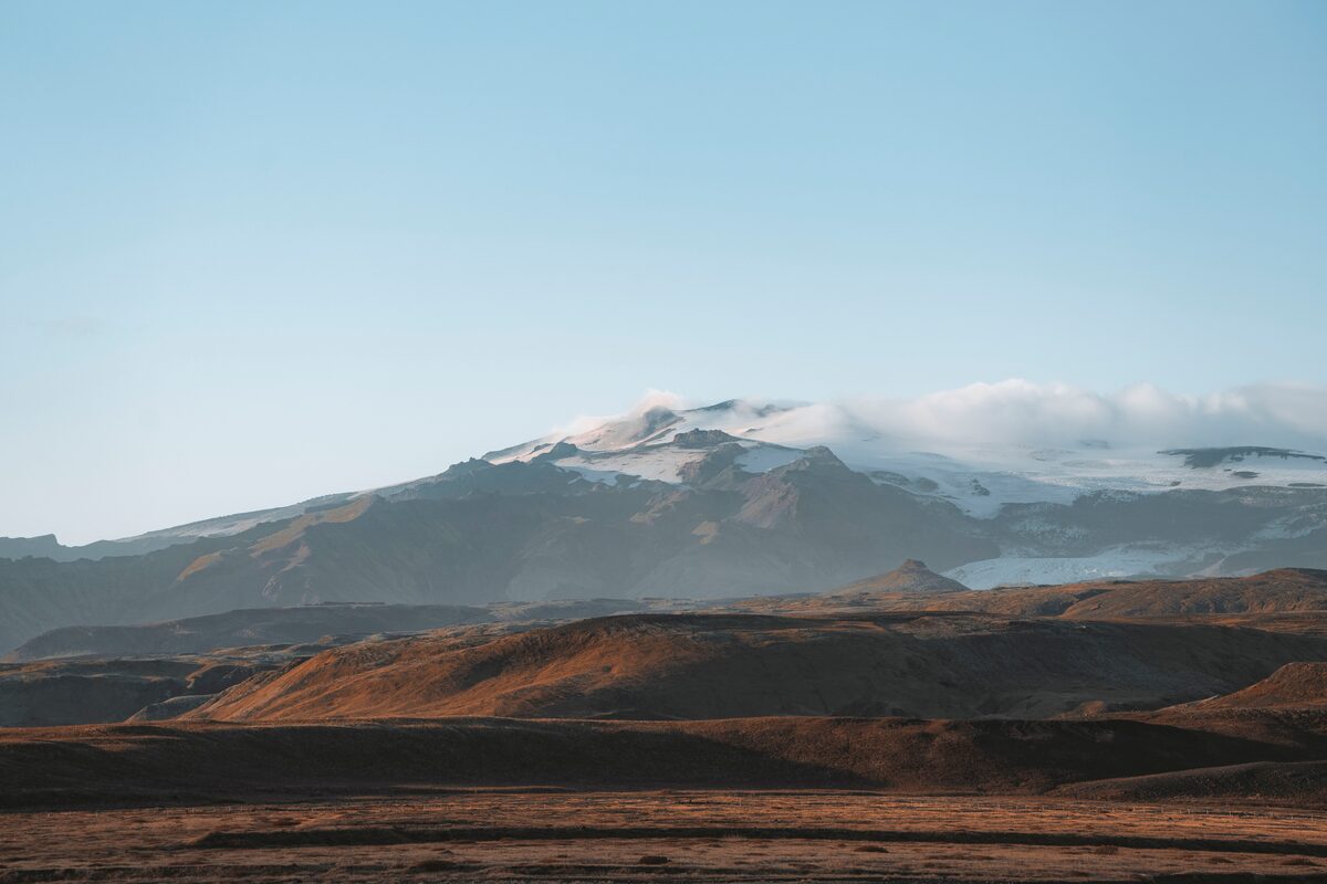 Red brown hills in landscape with snow covered mountain reaching clouds