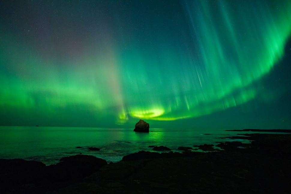 Majestic northern lights illuminating sky above sea and sandy black beach in foreground