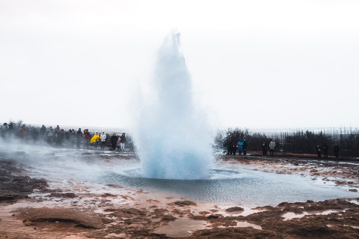 Light grey blue geothermal eruption and crowd standing around watching