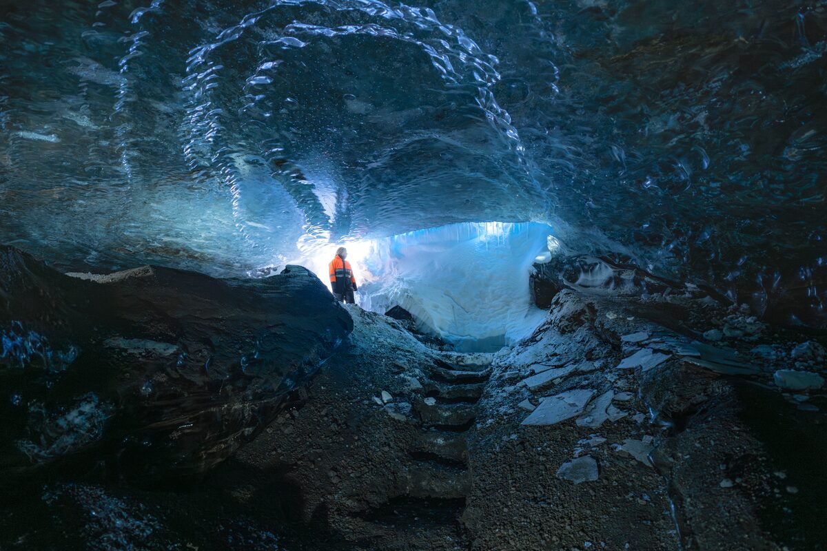 Tour guide in winter coat standing inside crystal like ice cave reflecting light inside
