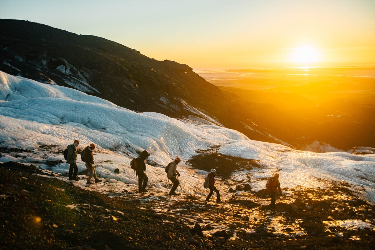 Group tour walking in line at Falljokull during golden sunset 
