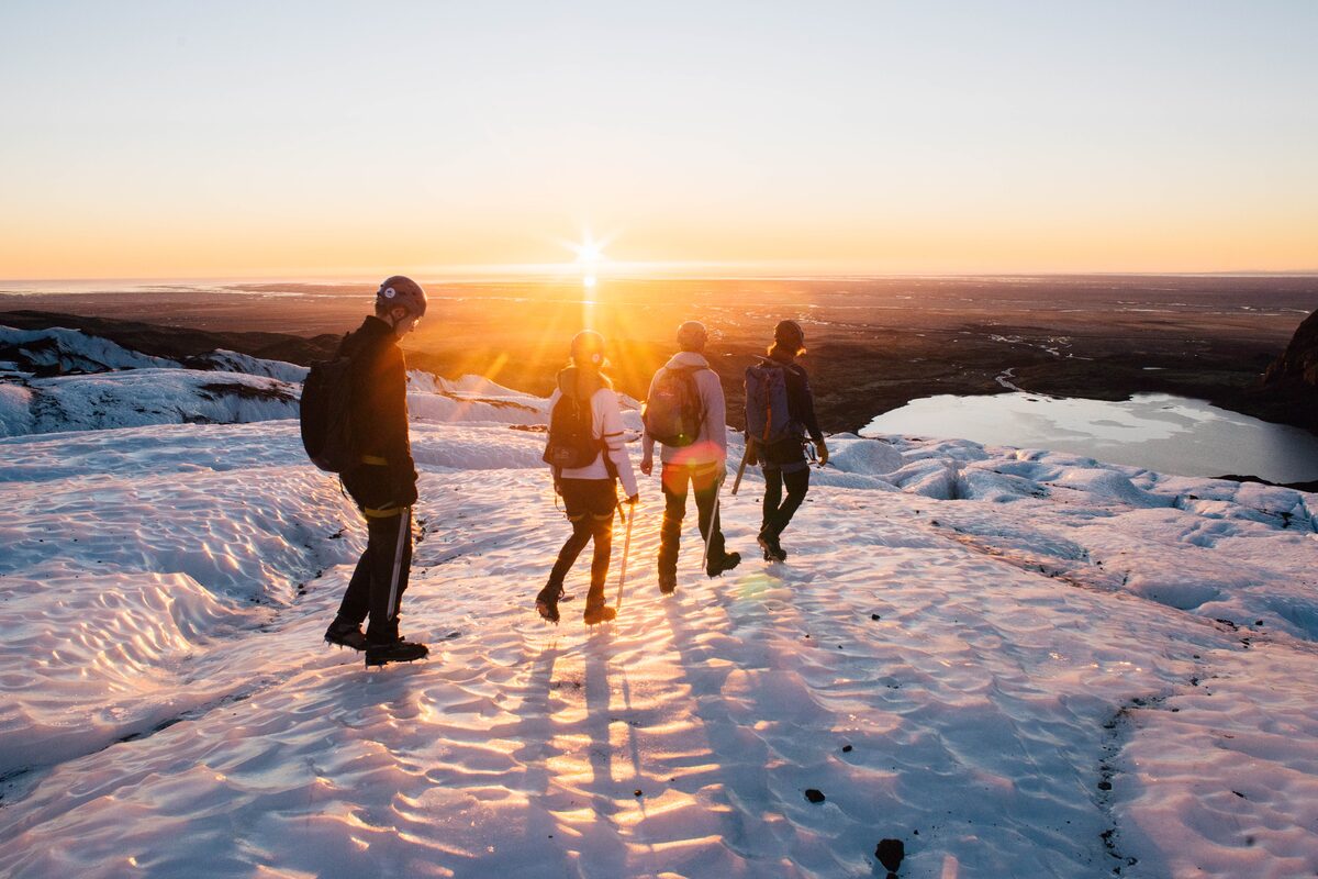 Four hikers walking along ice crevasses on glacier during bright golden sunset