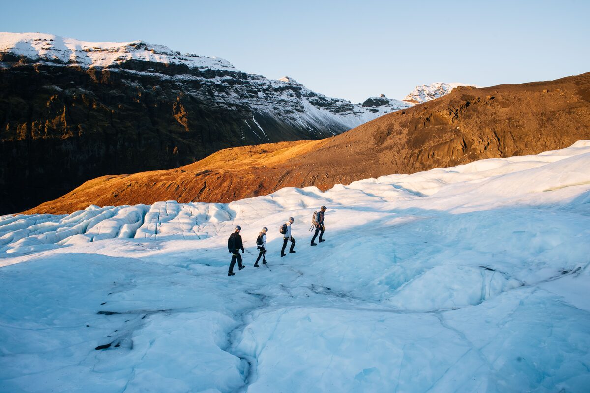 Four hikers walking across a glacier with beautiful mountains covered in snow