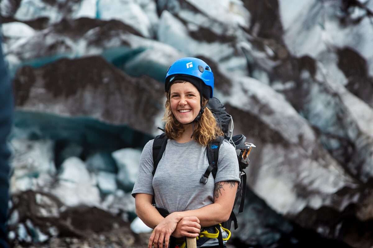 Female young tourist standing infront of blue and black formed ice crevasses on glacier