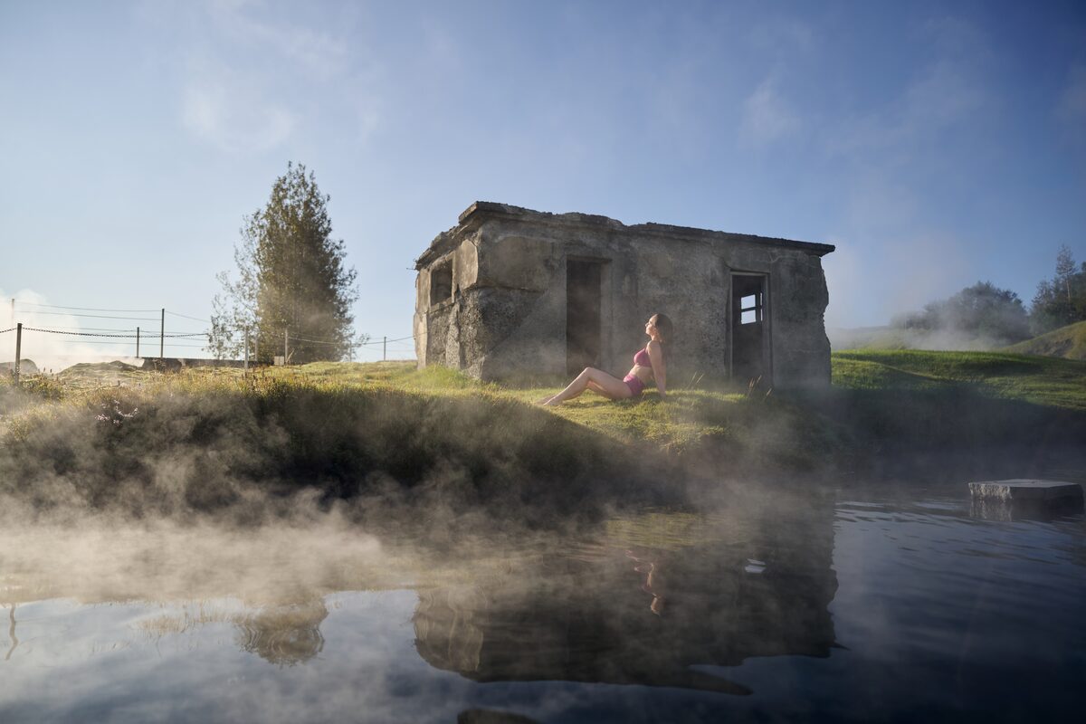 Lady sun bathing on grass sitting next to Secret Lagoon geothermal pool 