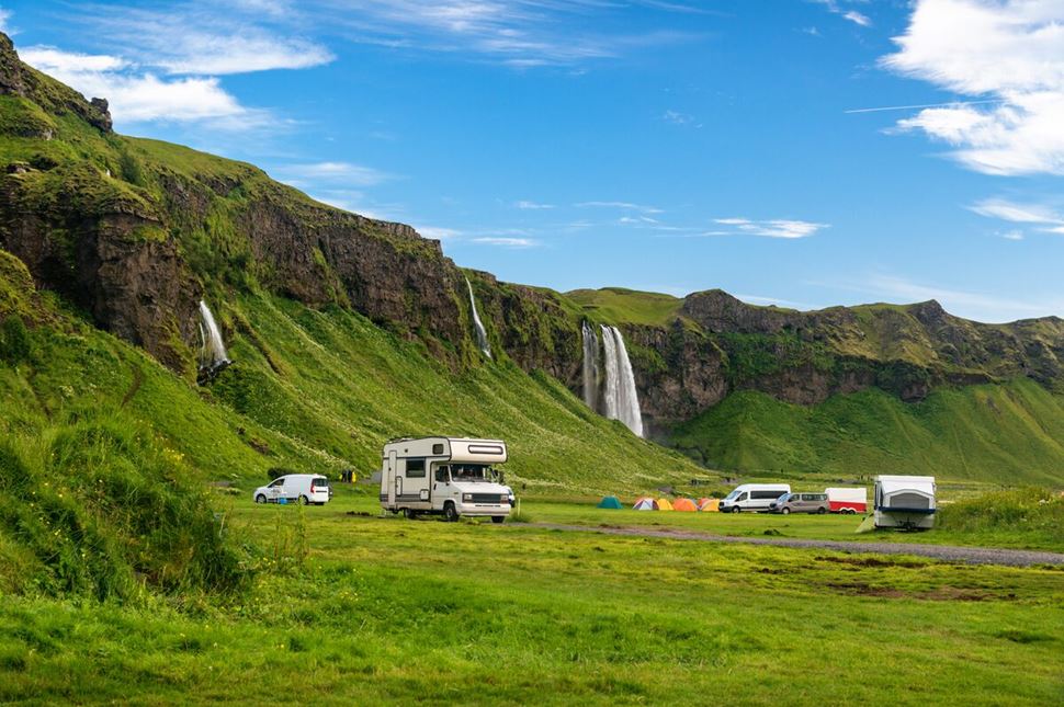 Camping van in summer on green field by huge waterfall in Iceland