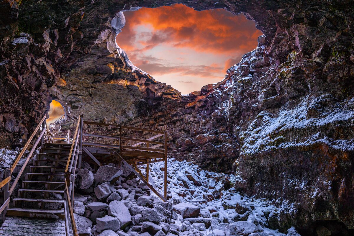 Inside Vidgelmir lava cave entrance snow covered with sunset lighting shining into cave