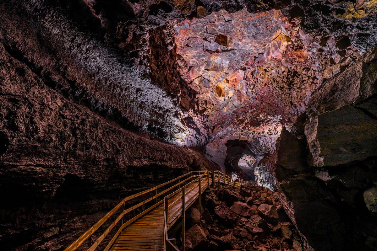 Walkway inside Vidgelmir lava cave with purple orange and pinkish cave interior