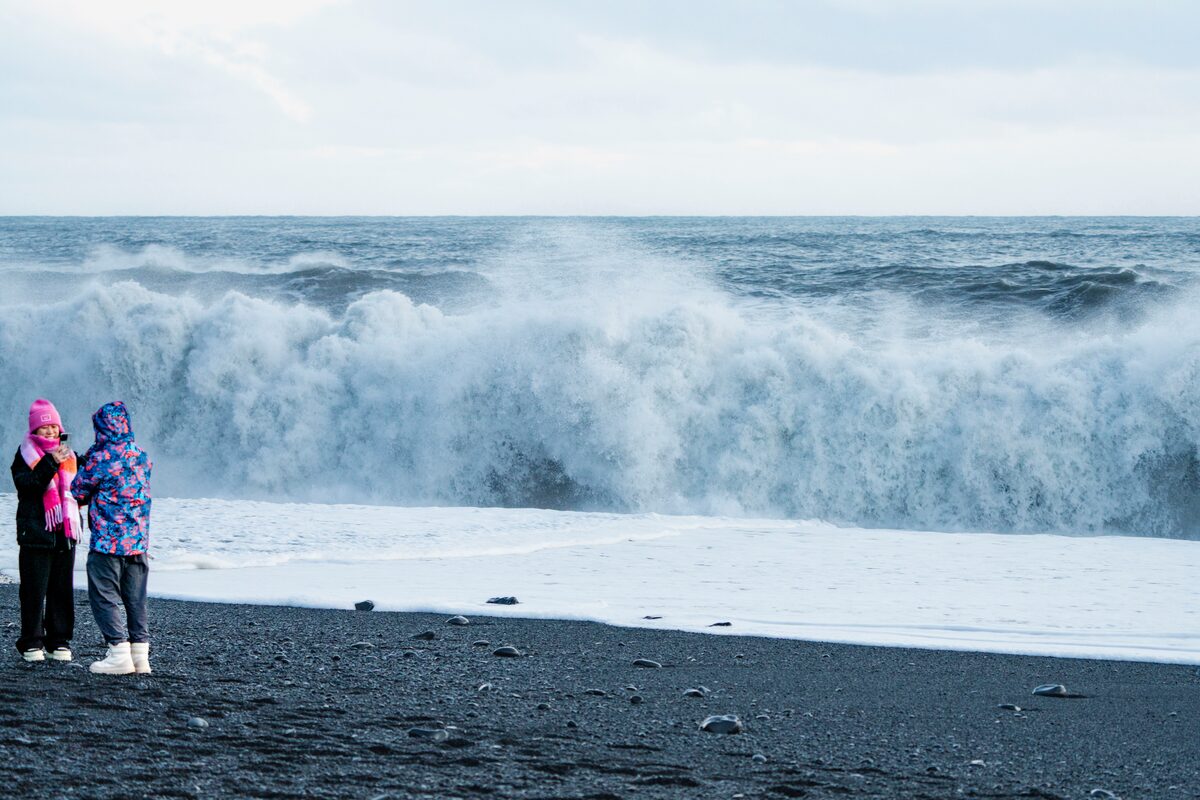 Couple standing at Reynisfjara beach with large crashing waves at shore