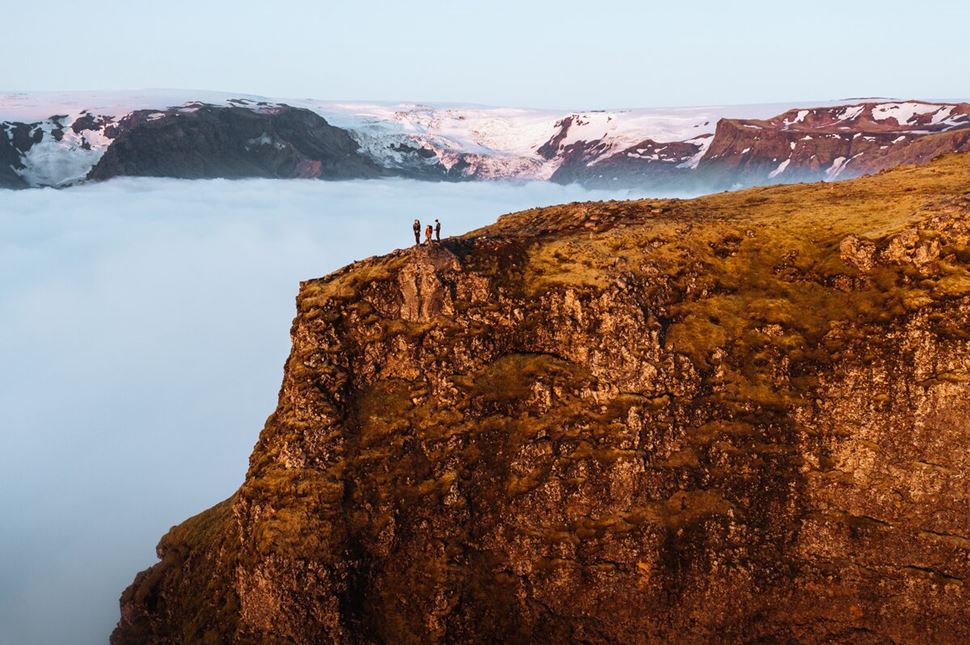 Group of three hikers standing on mountain edge surrounded by clouds
