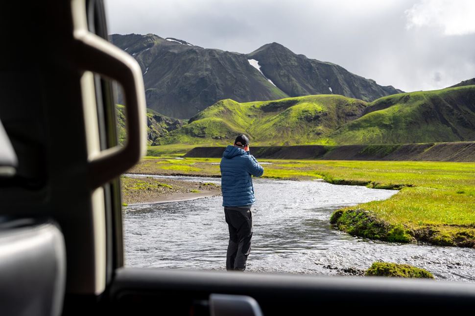 Hiker in blue jacket standing outside of car photographing stream on Laugavegur trail