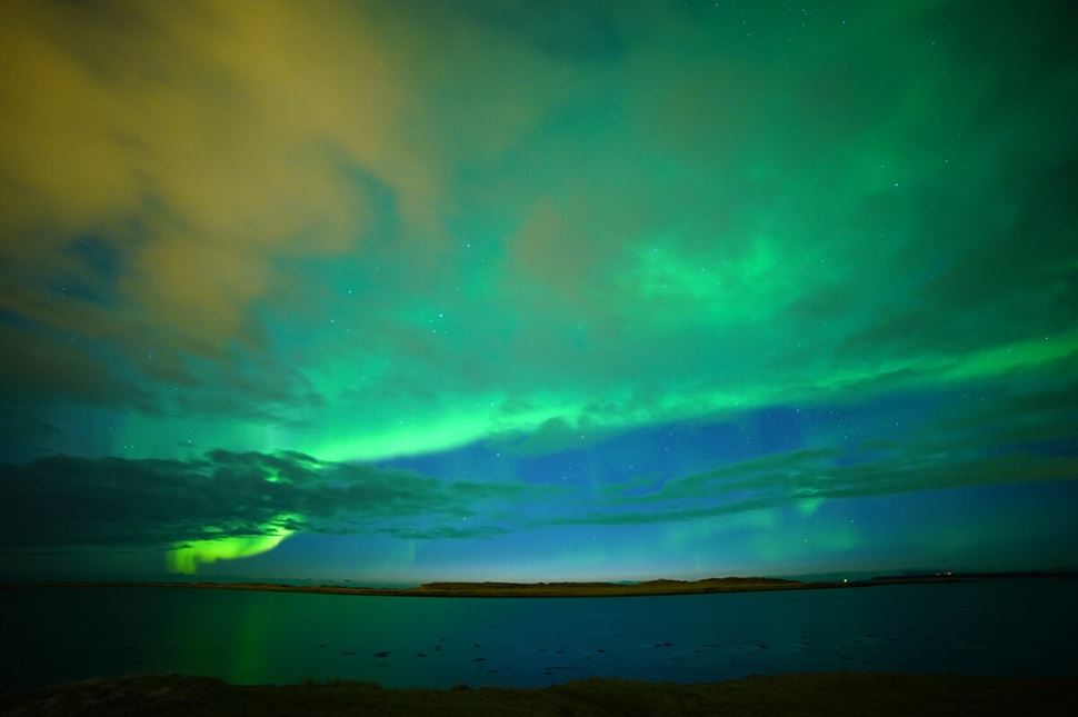 Blue and green northern lights in night sky over sea