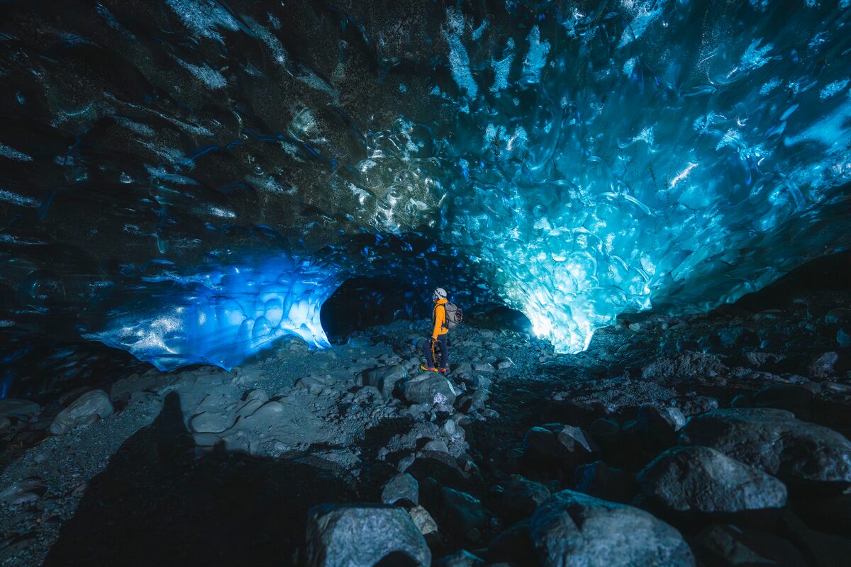 Tourist inside corner of the blue ice crystal cave with light reflecting showing patterns of ice cave walls.