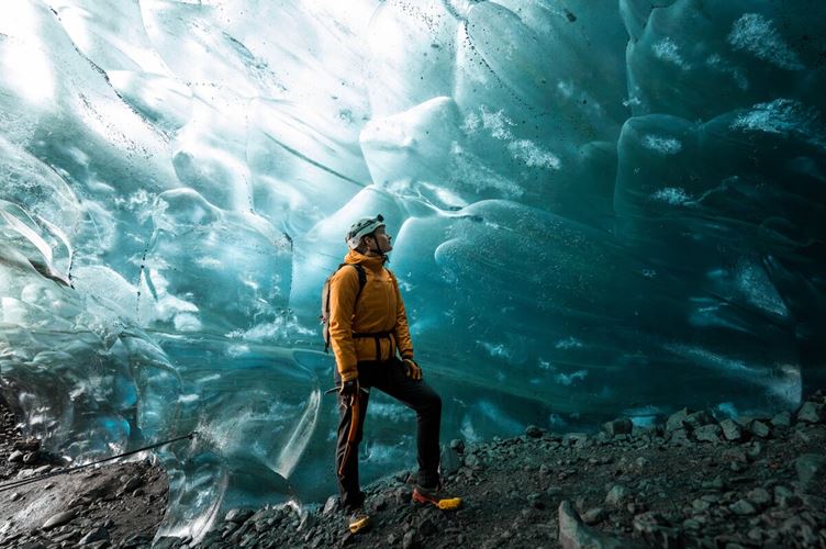 Male tourist wearing white safety hat admiring light shining off ice cave patterns