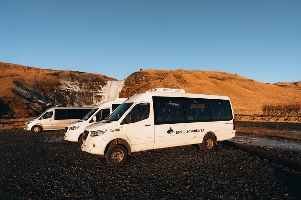 Arctic Adventures tour buses parked in front of Skogarfoss waterfall during autumn